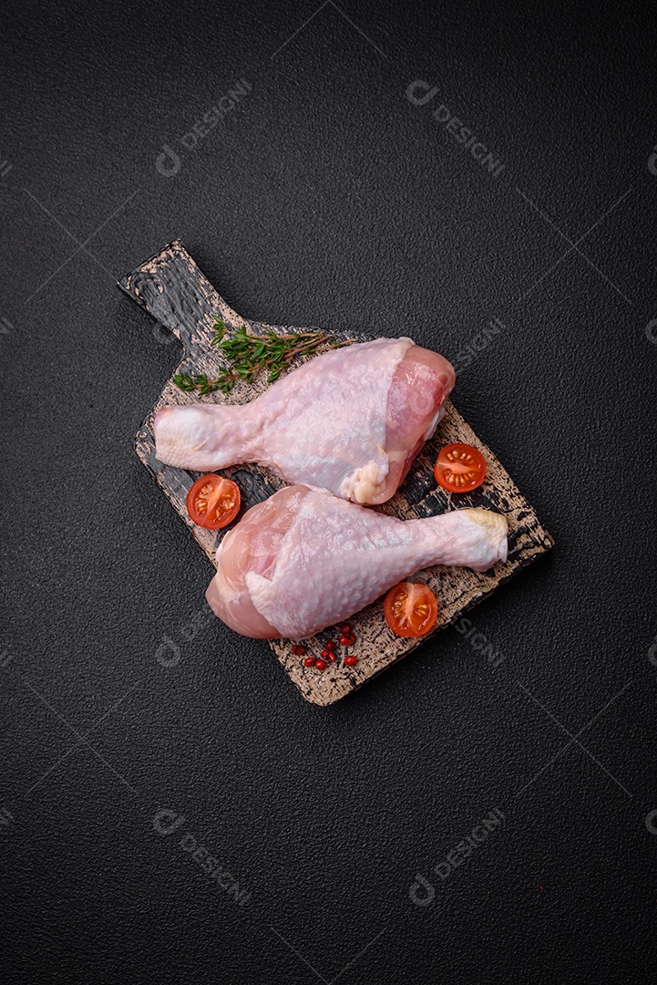 Pernas de frango cru com sal, especiarias e ervas sobre um fundo escuro de concreto. Cozinhando o almoço em casa