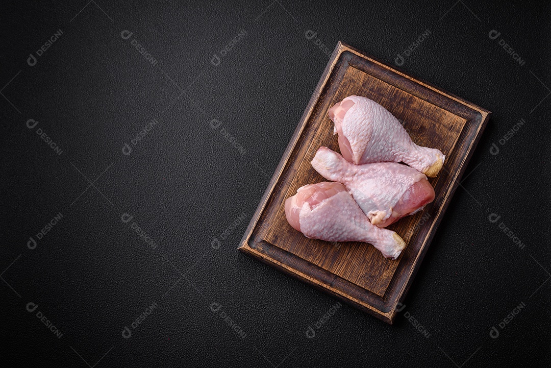 Pernas de frango cru com sal, especiarias e ervas sobre um fundo escuro de concreto. Cozinhando o almoço em casa