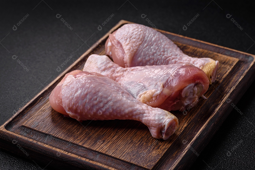 Pernas de frango cru com sal, especiarias e ervas sobre um fundo escuro de concreto. Cozinhando o almoço em casa