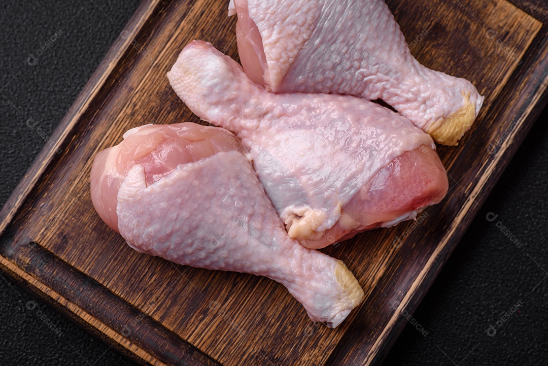 Pernas de frango cru com sal, especiarias e ervas sobre um fundo escuro de concreto. Cozinhando o almoço em casa