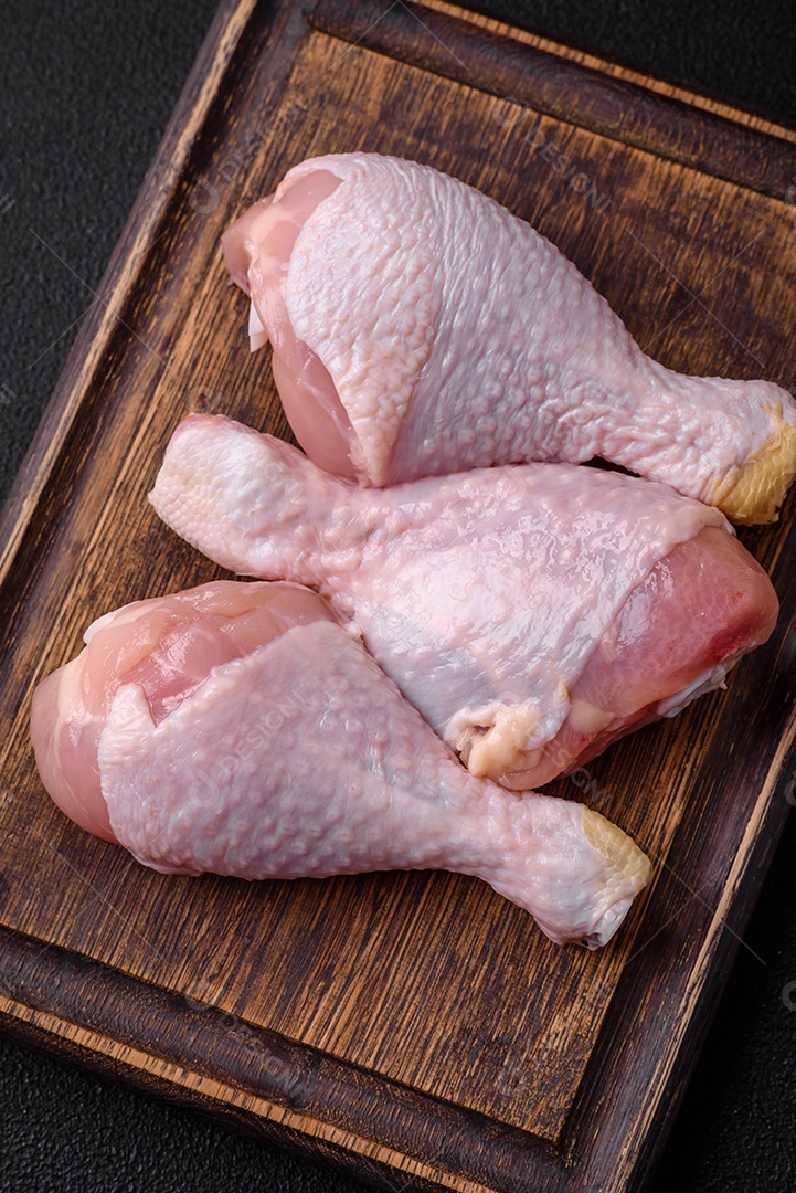 Pernas de frango cru com sal, especiarias e ervas sobre um fundo escuro de concreto. Cozinhando o almoço em casa