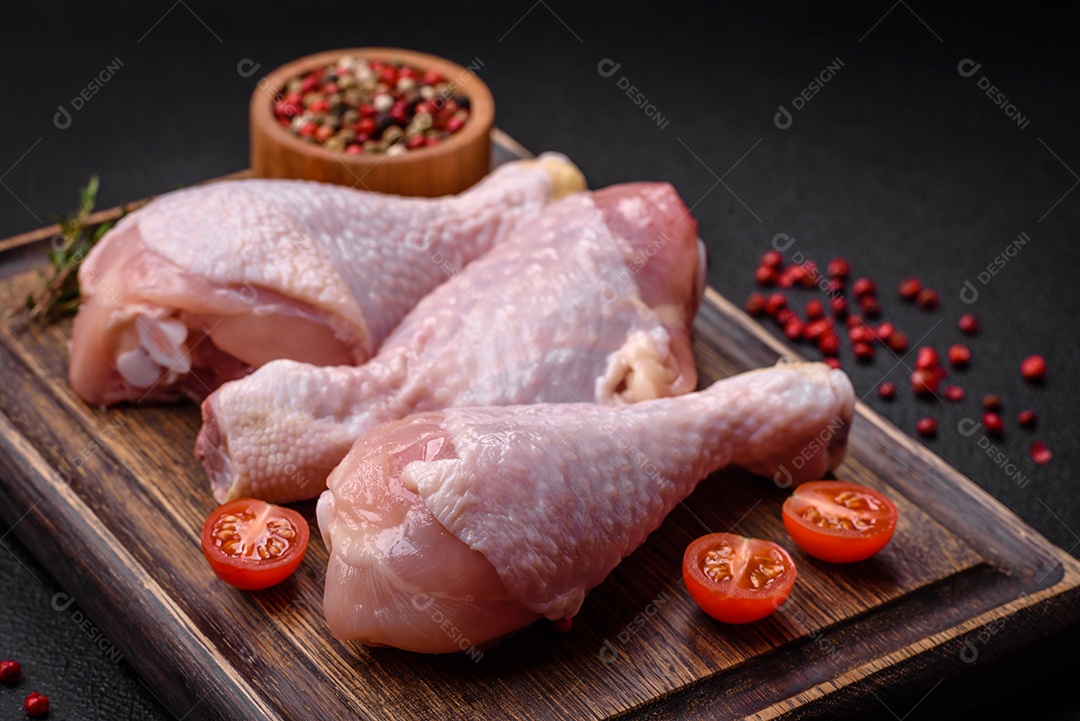 Pernas de frango cru com sal, especiarias e ervas sobre um fundo escuro de concreto. Cozinhando o almoço em casa