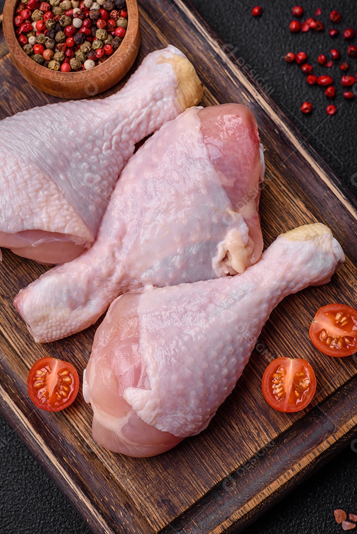 Pernas de frango cru com sal, especiarias e ervas sobre um fundo escuro de concreto. Cozinhando o almoço em casa