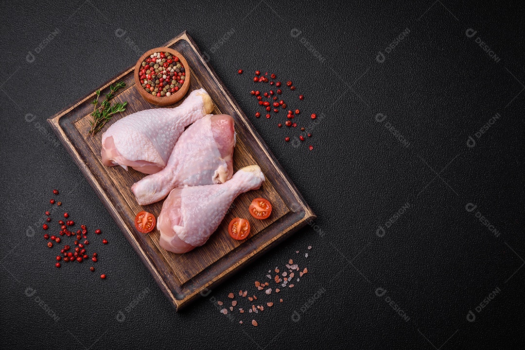 Pernas de frango cru com sal, especiarias e ervas sobre um fundo escuro de concreto. Cozinhando o almoço em casa