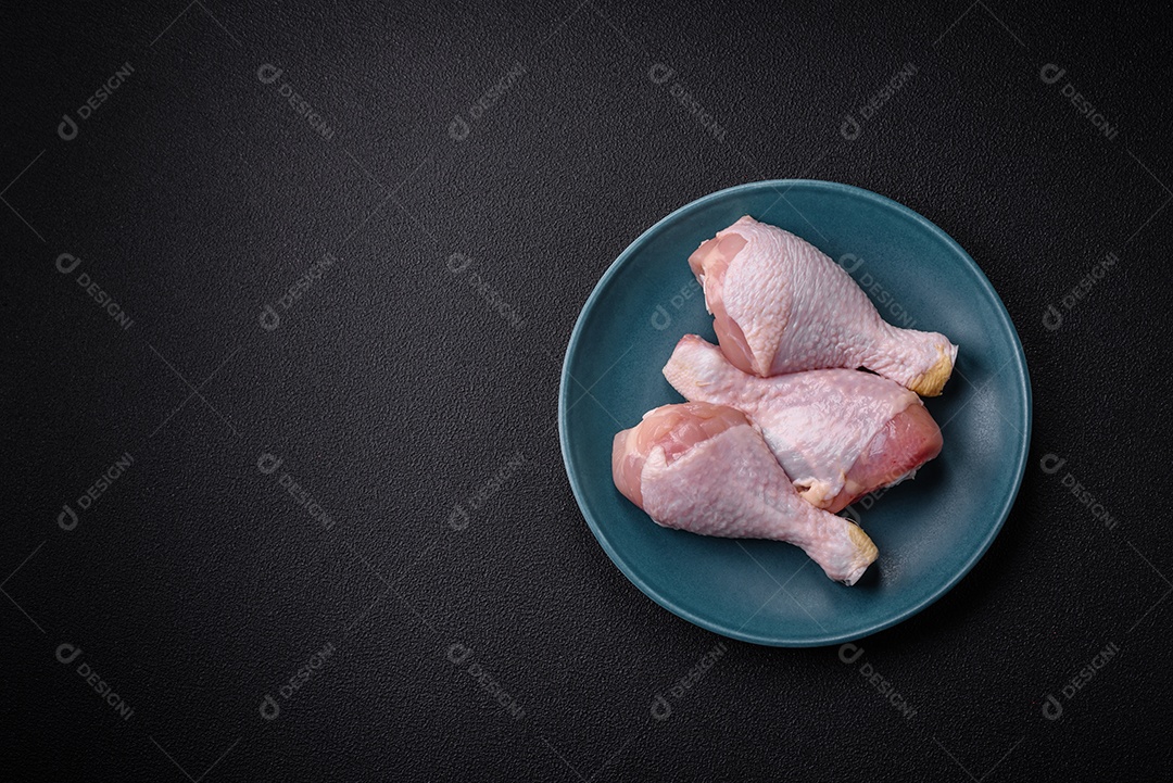 Pernas de frango cru com sal, especiarias e ervas sobre um fundo escuro de concreto. Cozinhando o almoço em casa