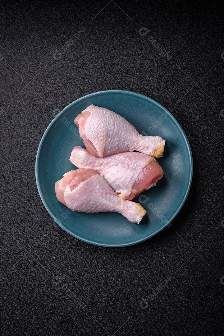 Pernas de frango cru com sal, especiarias e ervas sobre um fundo escuro de concreto. Cozinhando o almoço em casa