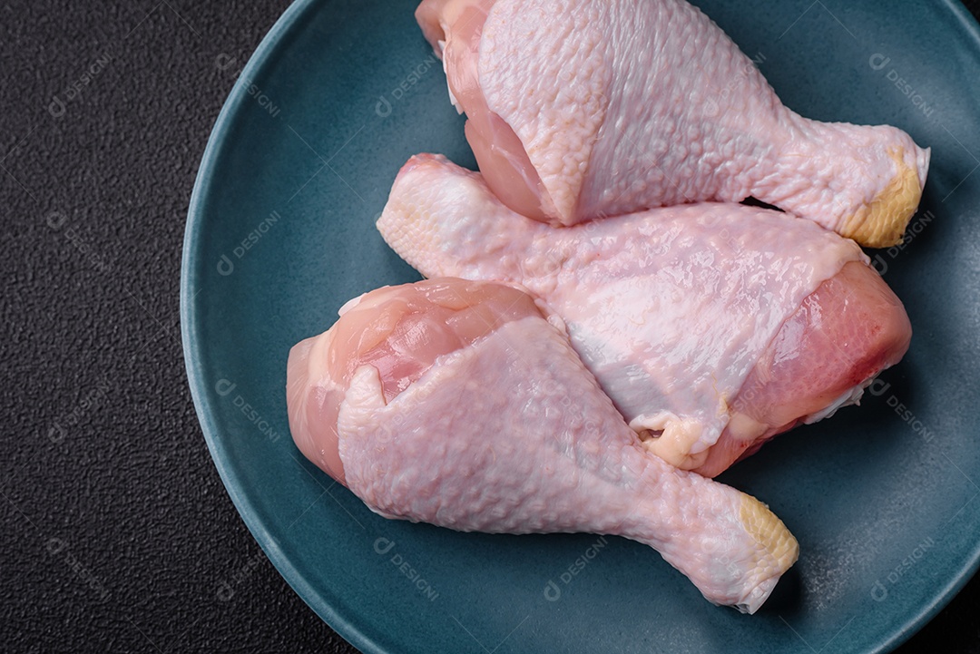 Pernas de frango cru com sal, especiarias e ervas sobre um fundo escuro de concreto. Cozinhando o almoço em casa
