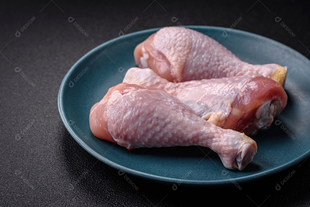Pernas de frango cru com sal, especiarias e ervas sobre um fundo escuro de concreto. Cozinhando o almoço em casa