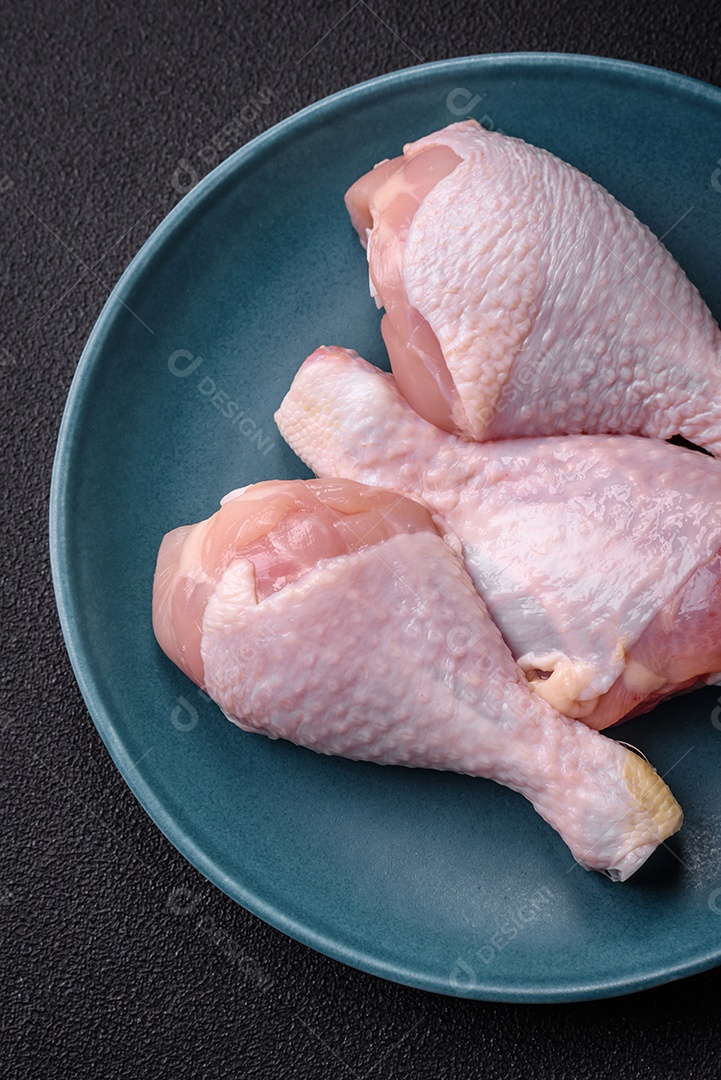 Pernas de frango cru com sal, especiarias e ervas sobre um fundo escuro de concreto. Cozinhando o almoço em casa