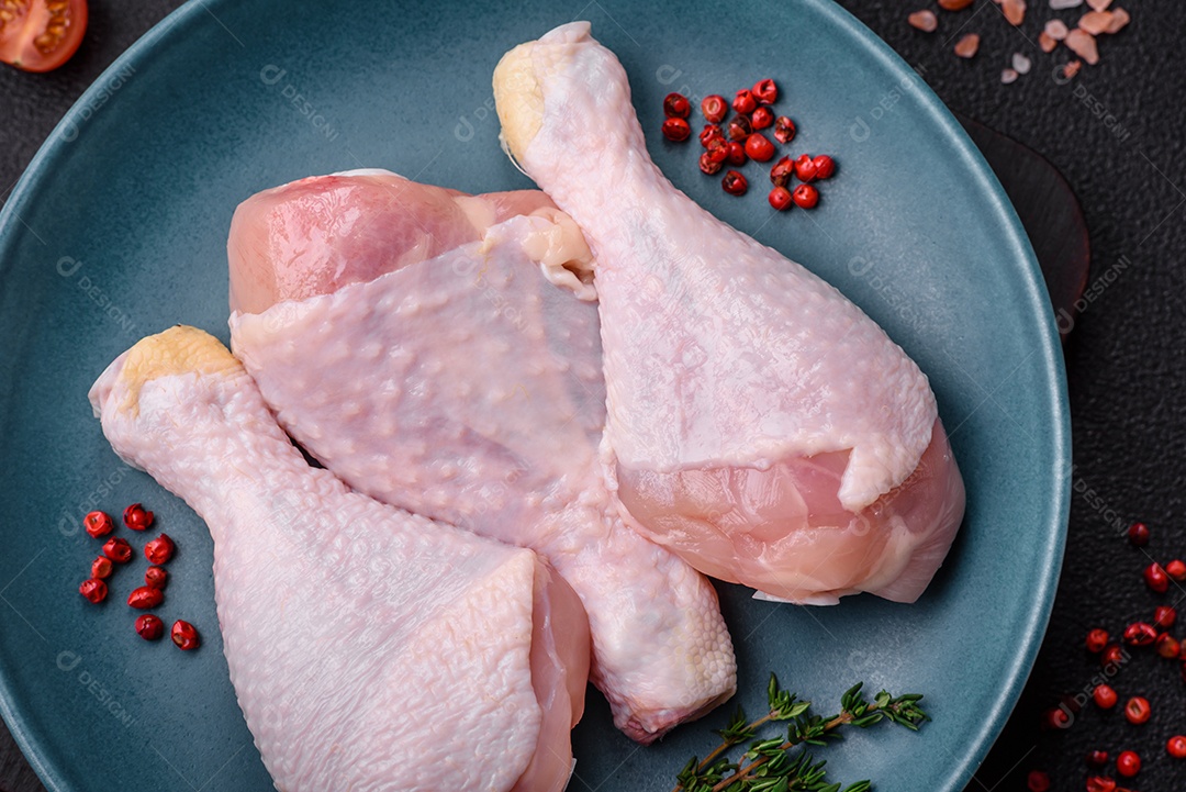 Pernas de frango cru com sal, especiarias e ervas sobre um fundo escuro de concreto. Cozinhando o almoço em casa