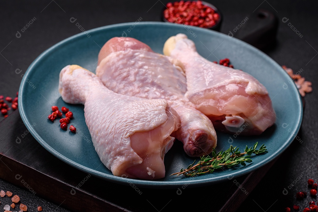 Pernas de frango cru com sal, especiarias e ervas sobre um fundo escuro de concreto. Cozinhando o almoço em casa