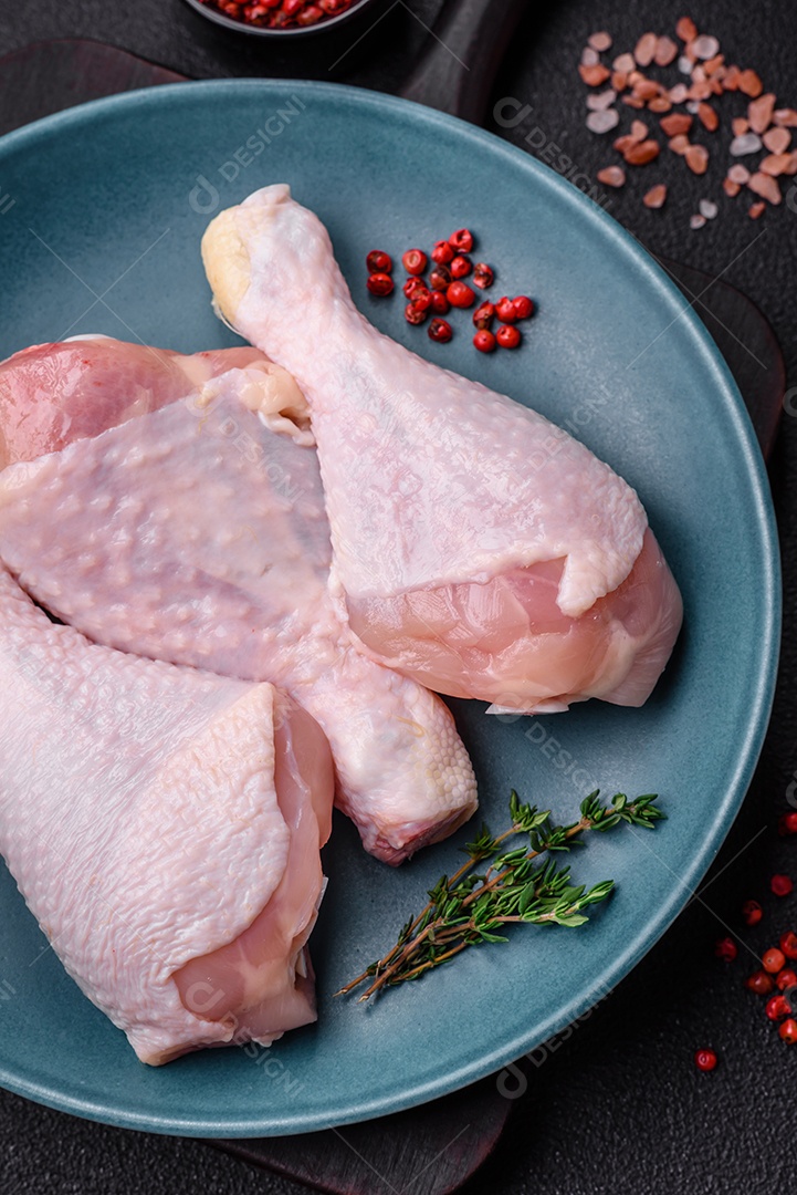 Pernas de frango cru com sal, especiarias e ervas sobre um fundo escuro de concreto. Cozinhando o almoço em casa