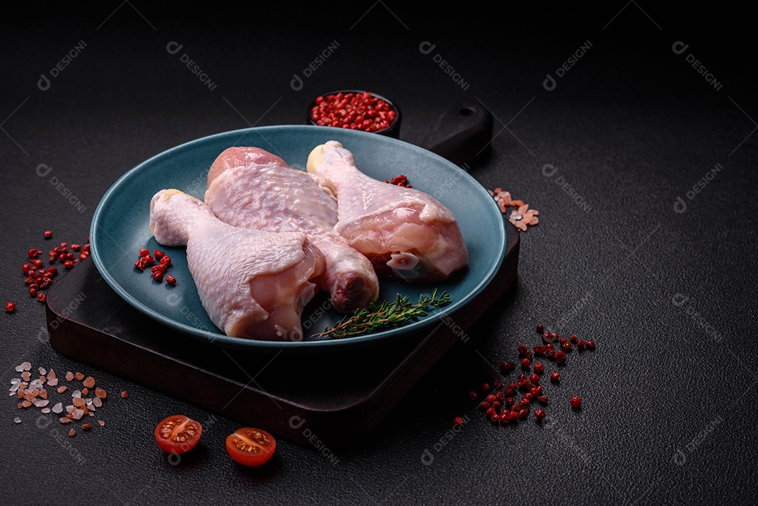 Pernas de frango cru com sal, especiarias e ervas sobre um fundo escuro de concreto. Cozinhando o almoço em casa