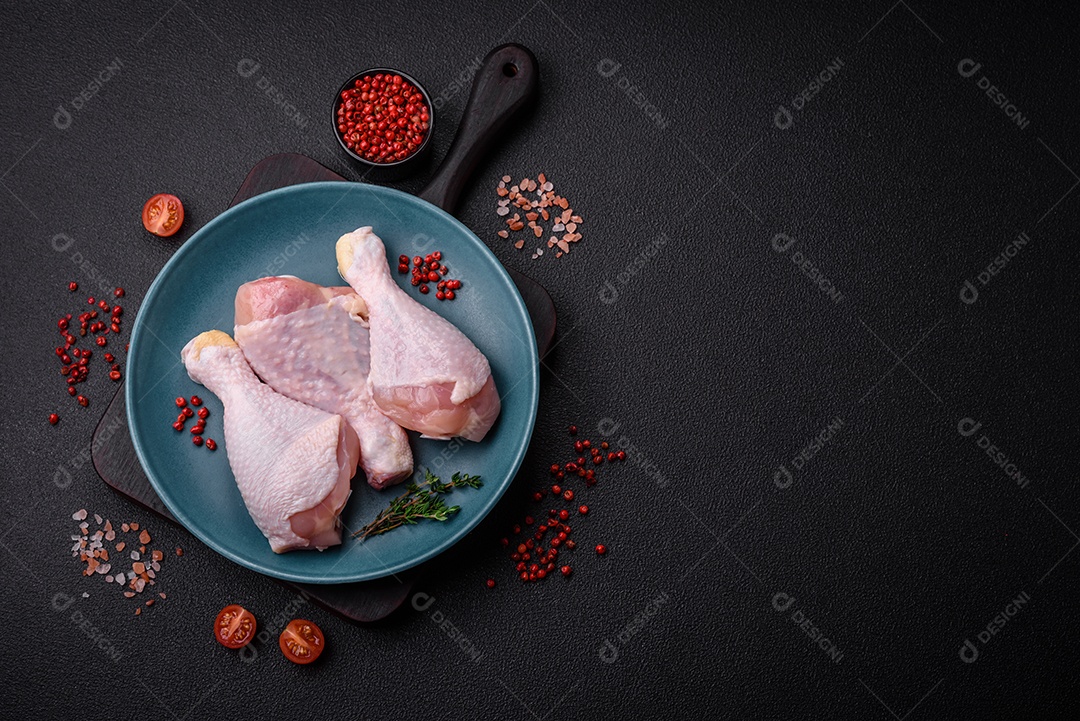Pernas de frango cru com sal, especiarias e ervas sobre um fundo escuro de concreto. Cozinhando o almoço em casa