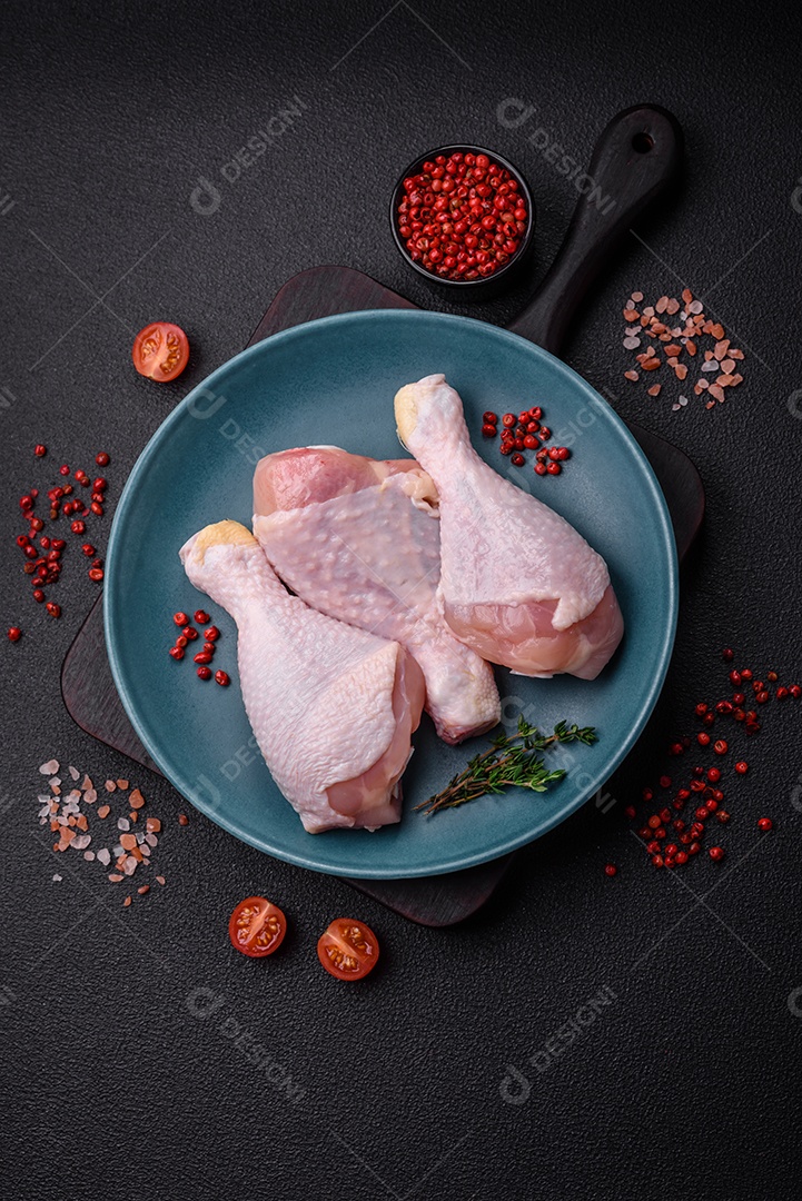 Pernas de frango cru com sal, especiarias e ervas sobre um fundo escuro de concreto. Cozinhando o almoço em casa