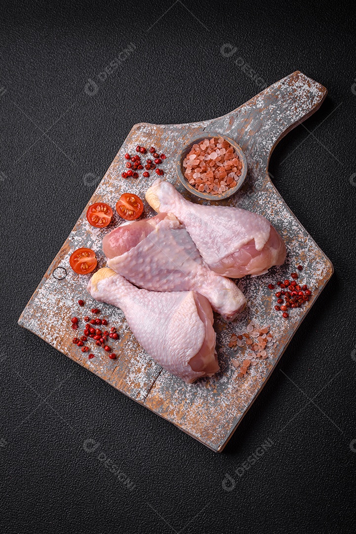 Pernas de frango cru com sal, especiarias e ervas sobre um fundo escuro de concreto. Cozinhando o almoço em casa