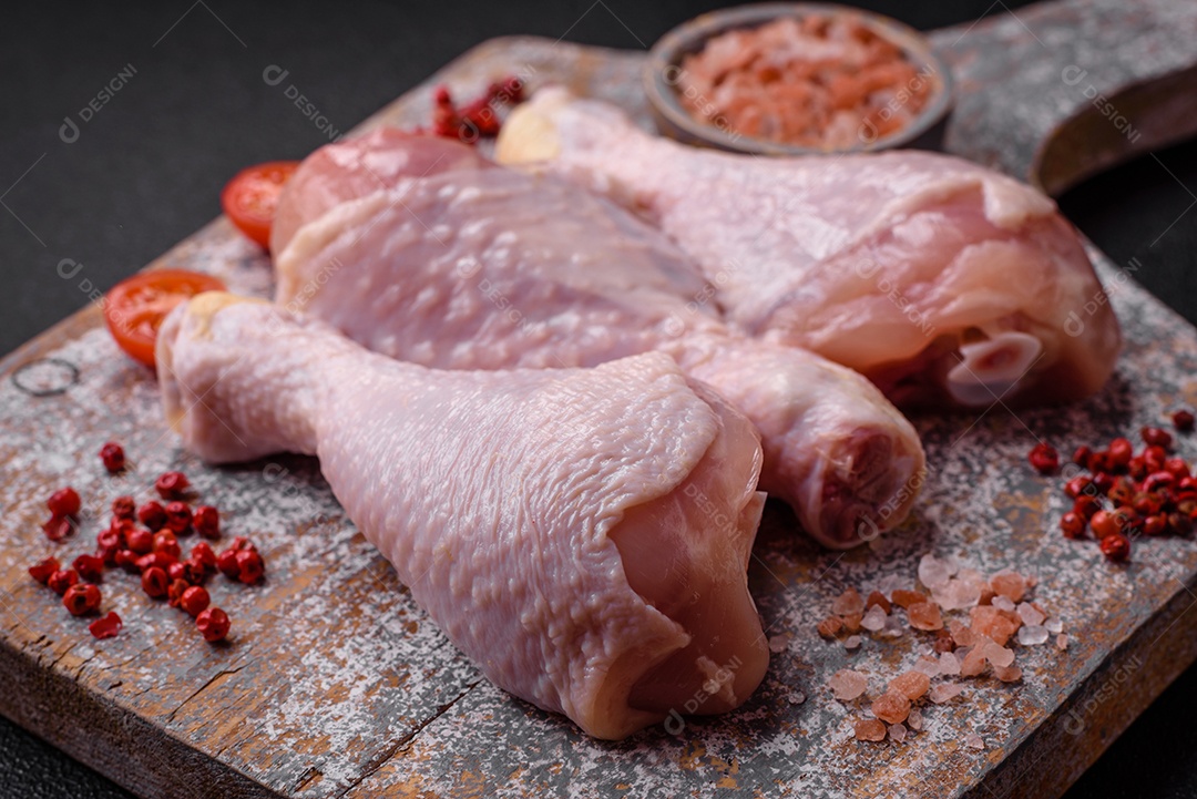 Pernas de frango cru com sal, especiarias e ervas sobre um fundo escuro de concreto. Cozinhando o almoço em casa