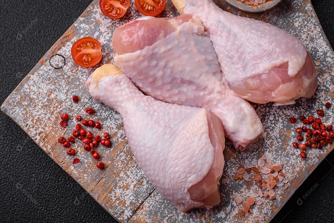 Pernas de frango cru com sal, especiarias e ervas sobre um fundo escuro de concreto. Cozinhando o almoço em casa