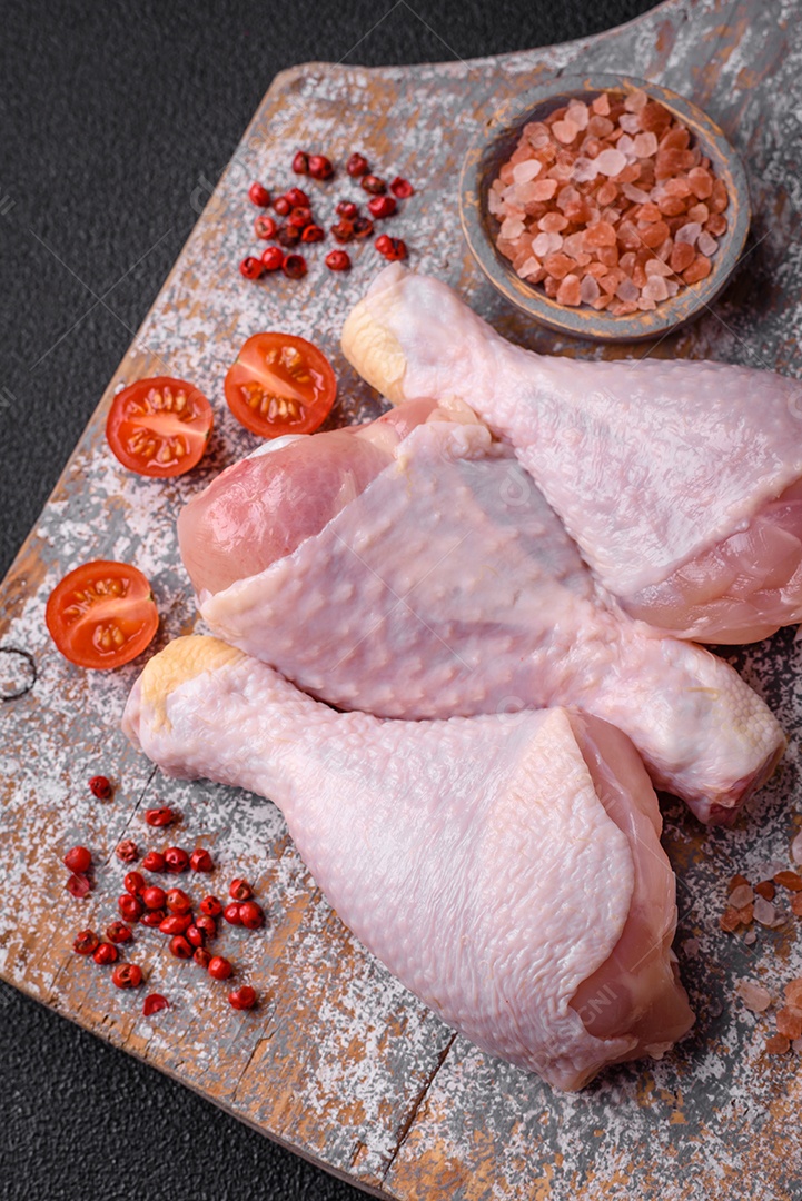 Pernas de frango cru com sal, especiarias e ervas sobre um fundo escuro de concreto. Cozinhando o almoço em casa