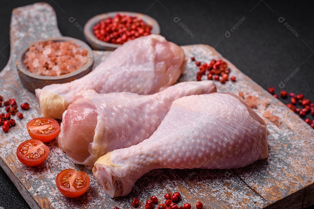 Pernas de frango cru com sal, especiarias e ervas sobre um fundo escuro de concreto. Cozinhando o almoço em casaPernas de frango cru com sal, especiarias e ervas sobre um fundo escuro de concreto. Cozinhando o almoço em casa