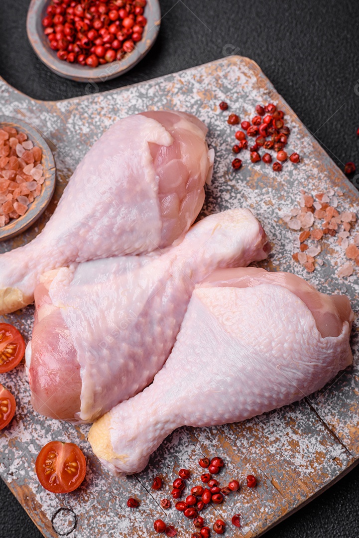 Pernas de frango cru com sal, especiarias e ervas sobre um fundo escuro de concreto. Cozinhando o almoço em casa