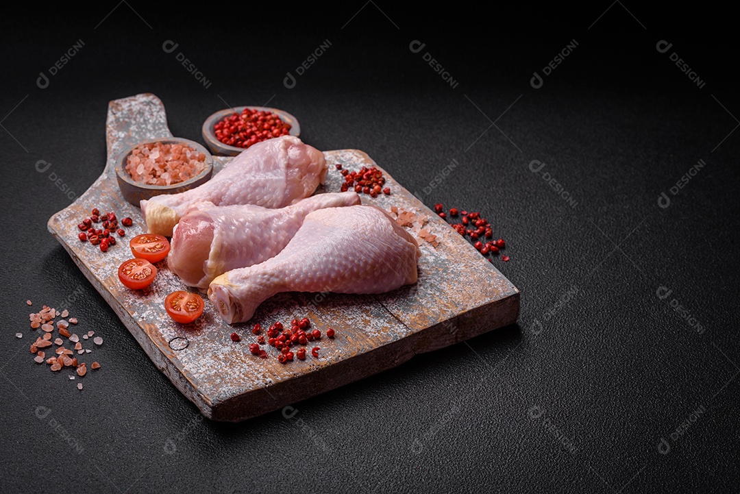 Pernas de frango cru com sal, especiarias e ervas sobre um fundo escuro de concreto. Cozinhando o almoço em casa