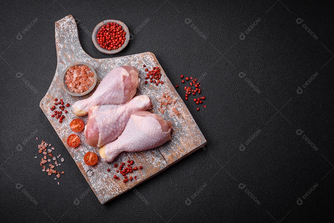 Pernas de frango cru com sal, especiarias e ervas sobre um fundo escuro de concreto. Cozinhando o almoço em casa