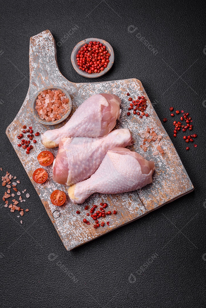 Pernas de frango cru com sal, especiarias e ervas sobre um fundo escuro de concreto. Cozinhando o almoço em casa