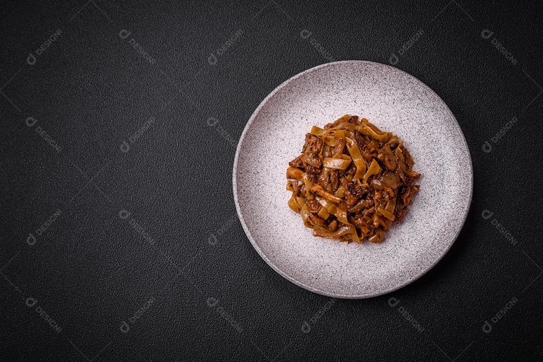 Delicioso prato de udon asiático com legumes, cogumelos, sal e especiarias numa placa cerâmica sobre um fundo escuro de concreto