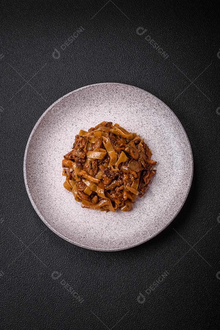 Delicioso prato de udon asiático com legumes, cogumelos, sal e especiarias numa placa cerâmica sobre um fundo escuro de concreto