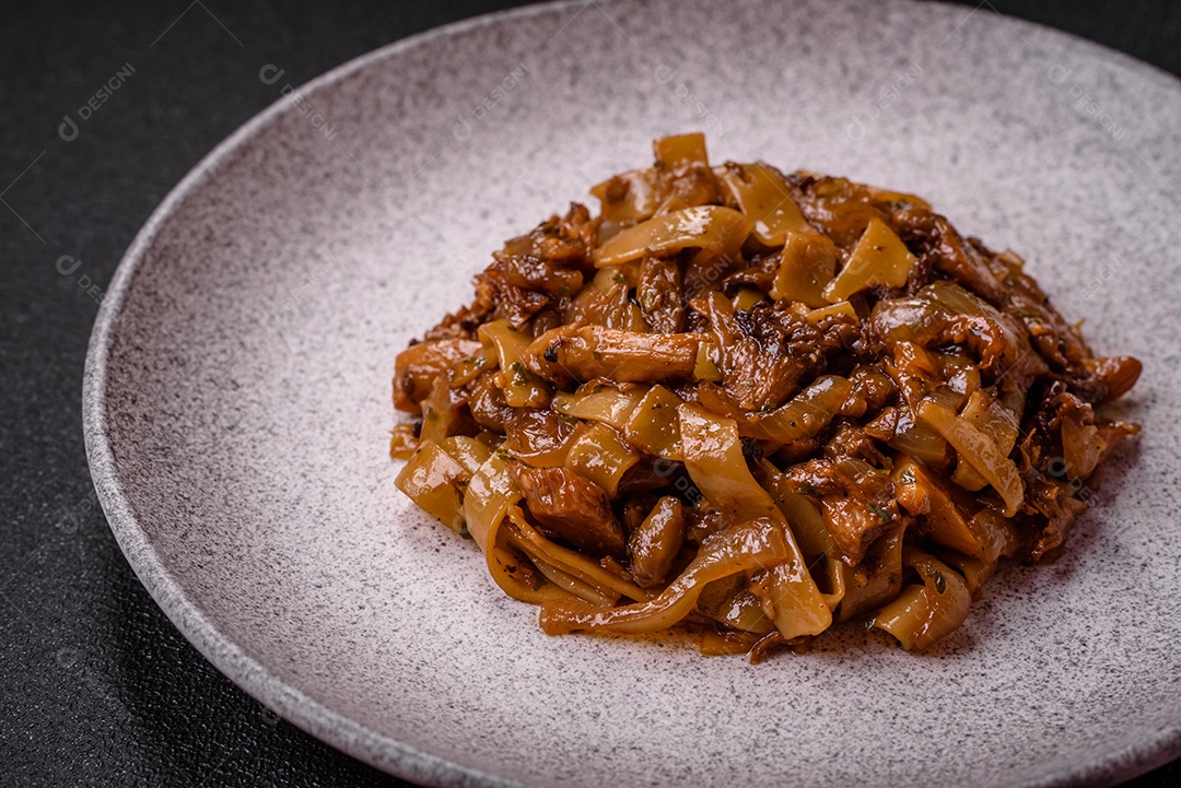 Delicioso prato de udon asiático com legumes, cogumelos, sal e especiarias numa placa cerâmica sobre um fundo escuro de concreto