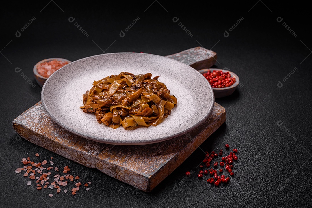 Delicioso prato de udon asiático com legumes, cogumelos, sal e especiarias numa placa cerâmica sobre um fundo escuro de concreto