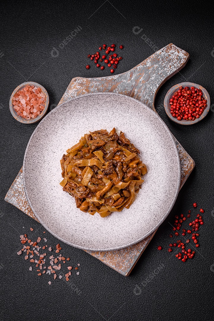 Delicioso prato de udon asiático com legumes, cogumelos, sal e especiarias numa placa cerâmica sobre um fundo escuro de concreto