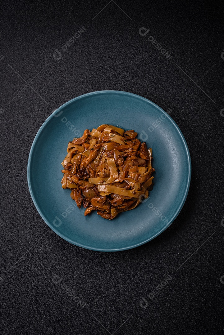 Delicioso prato de udon asiático com legumes, cogumelos, sal e especiarias numa placa cerâmica sobre um fundo escuro de concreto