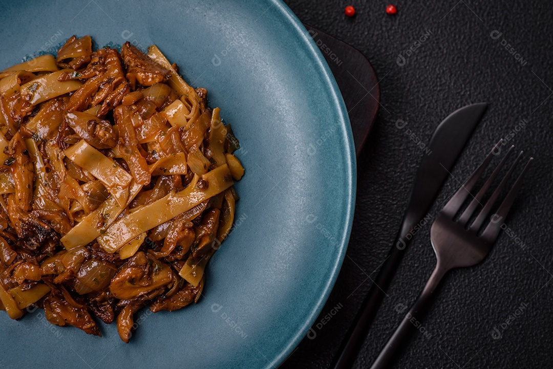 Delicioso prato de udon asiático com legumes, cogumelos, sal e especiarias numa placa cerâmica sobre um fundo escuro de concreto