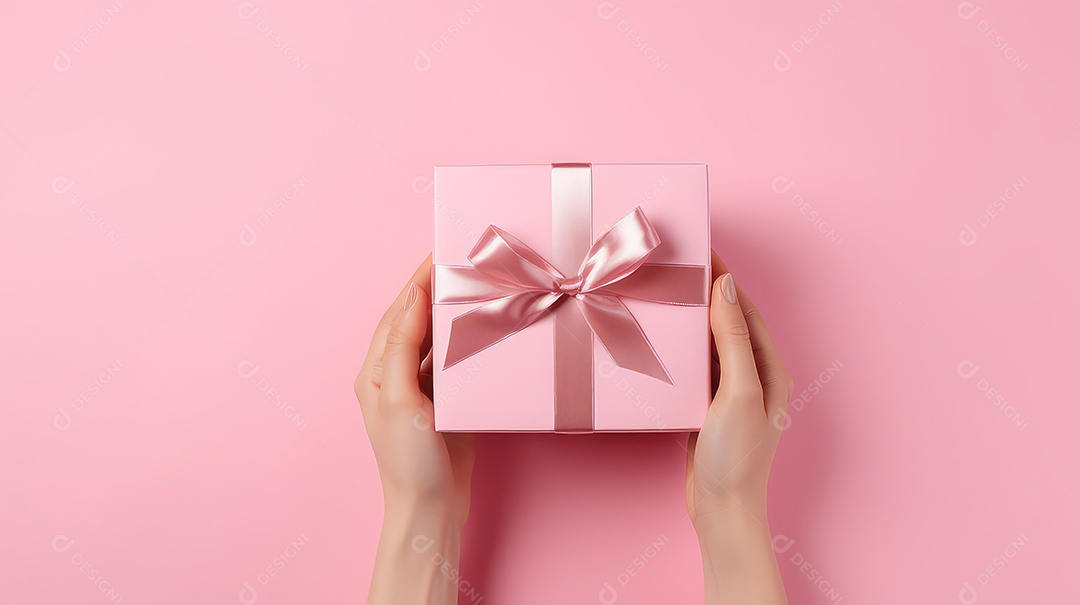Mãos femininas segurando uma caixa de presente rosa em um fundo rosa