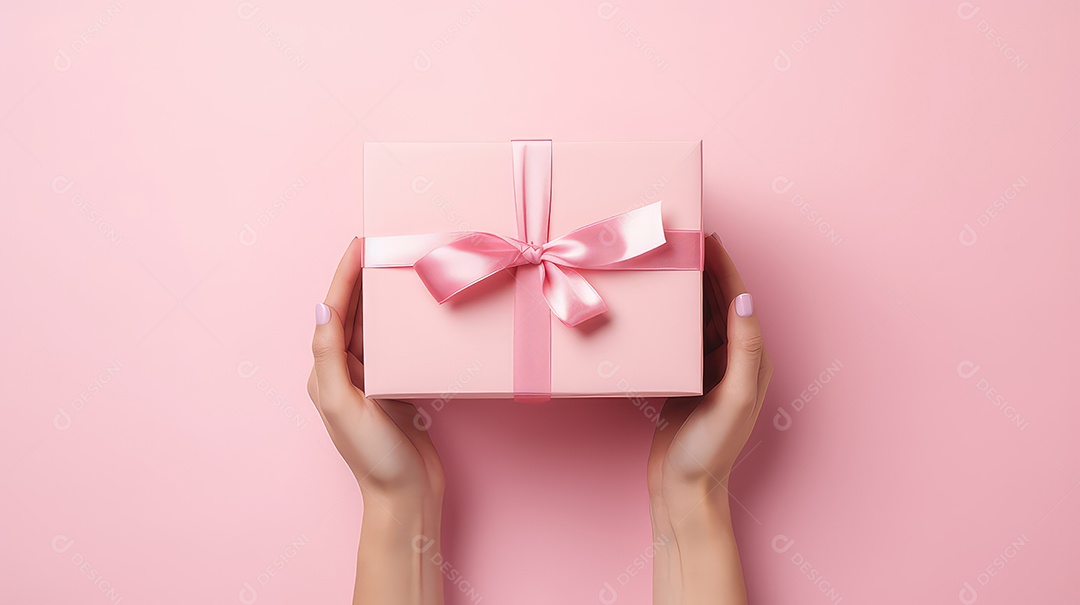 Mãos femininas segurando uma caixa de presente rosa em um fundo rosa