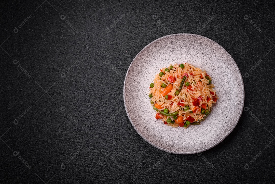 Delicioso arroz cozido com legumes, pimentas, ervilhas verdes, sal, especiarias e ervas sobre um fundo escuro de concreto