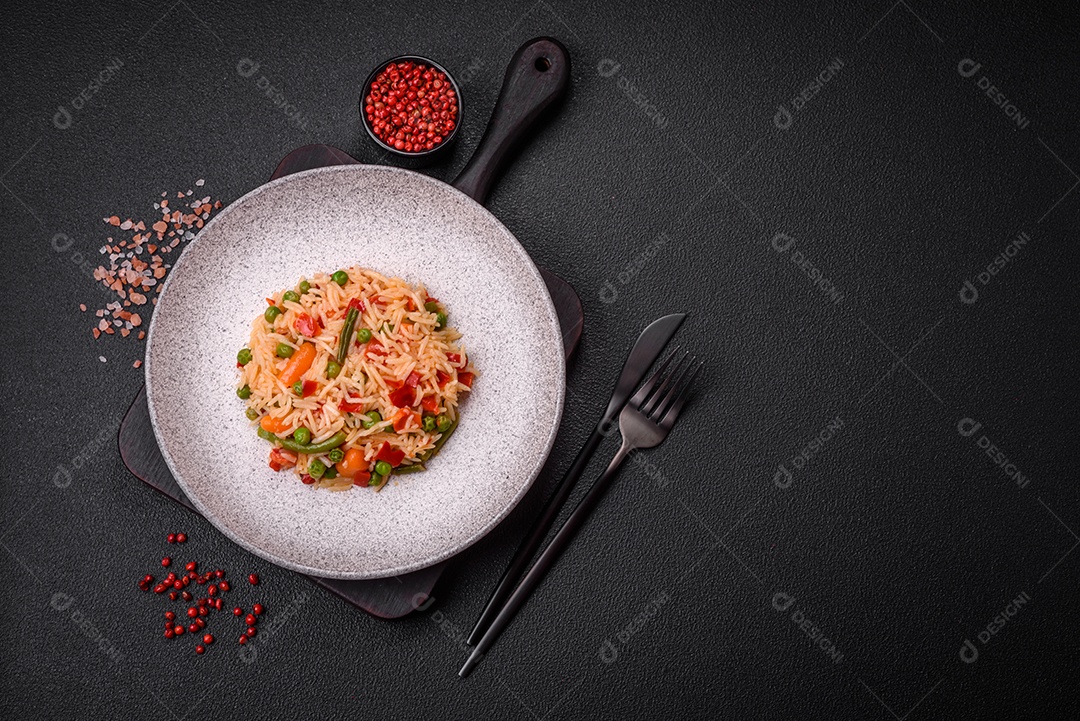 Delicioso arroz cozido com legumes, pimentas, ervilhas verdes, sal, especiarias e ervas sobre um fundo escuro de concreto