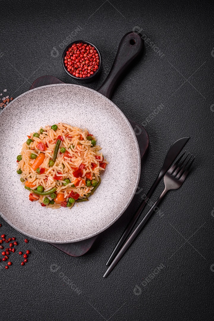 Delicioso arroz cozido com legumes, pimentas, ervilhas verdes, sal, especiarias e ervas sobre um fundo escuro de concreto