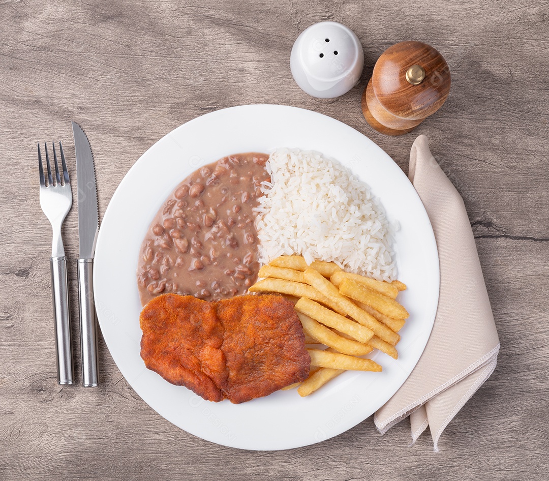 Carne à milanesa arroz feijão e batata frita temperos e talheres sobre fundo de pedra