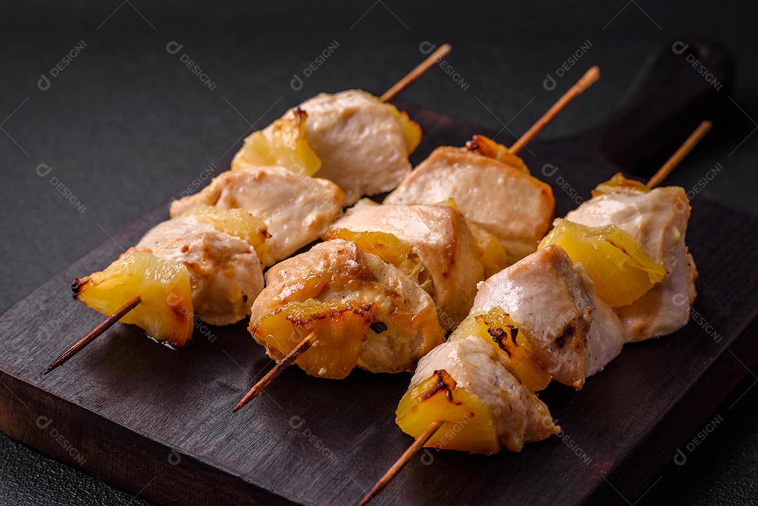 Delicioso kebab de frango ou peru com pedaços de abacaxi em espetos com sal, especiarias e ervas em um fundo escuro de concreto