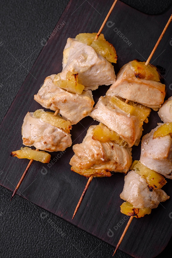 Delicioso kebab de frango ou peru com pedaços de abacaxi em espetos com sal, especiarias e ervas em um fundo escuro de concreto
