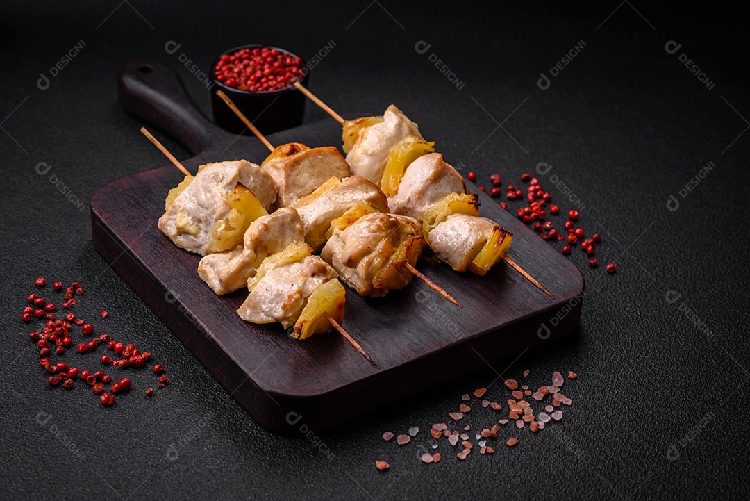 Delicioso kebab de frango ou peru com pedaços de abacaxi em espetos com sal, especiarias e ervas em um fundo escuro de concreto