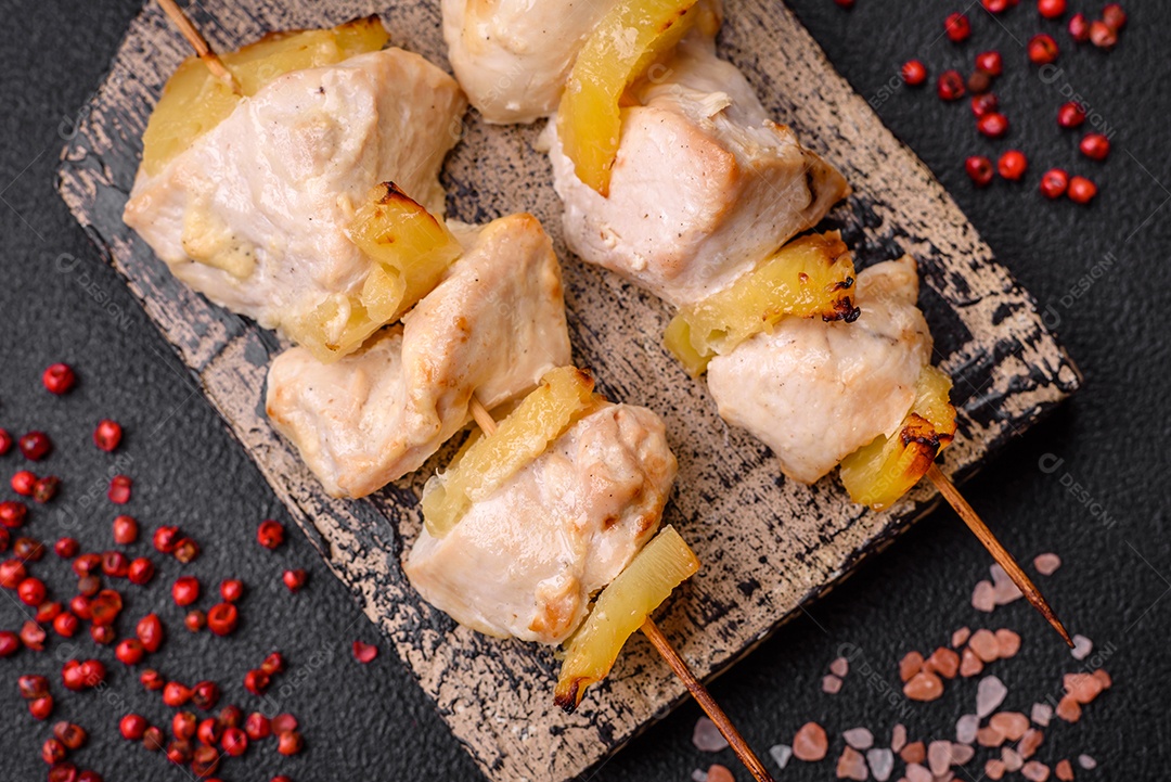 Delicioso kebab de frango ou peru com pedaços de abacaxi em espetos com sal, especiarias e ervas em um fundo escuro de concreto