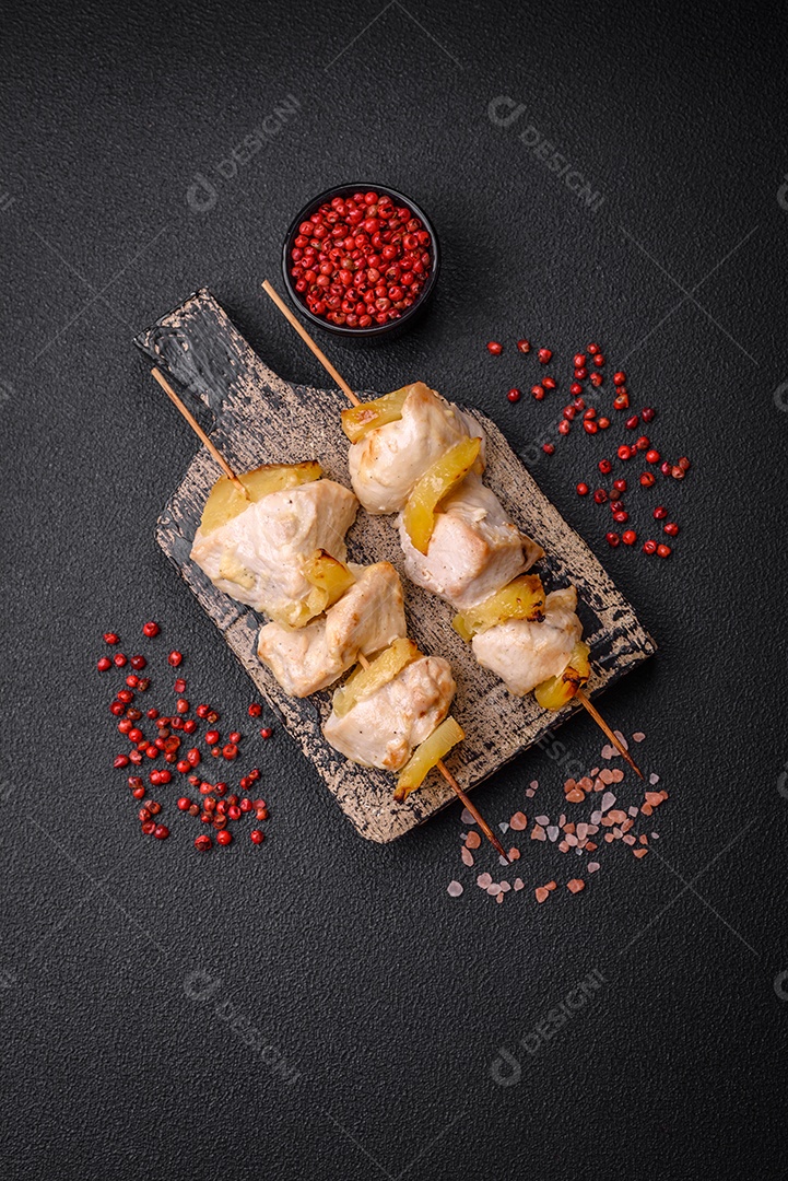 Delicioso kebab de frango ou peru com pedaços de abacaxi em espetos com sal, especiarias e ervas em um fundo escuro de concreto