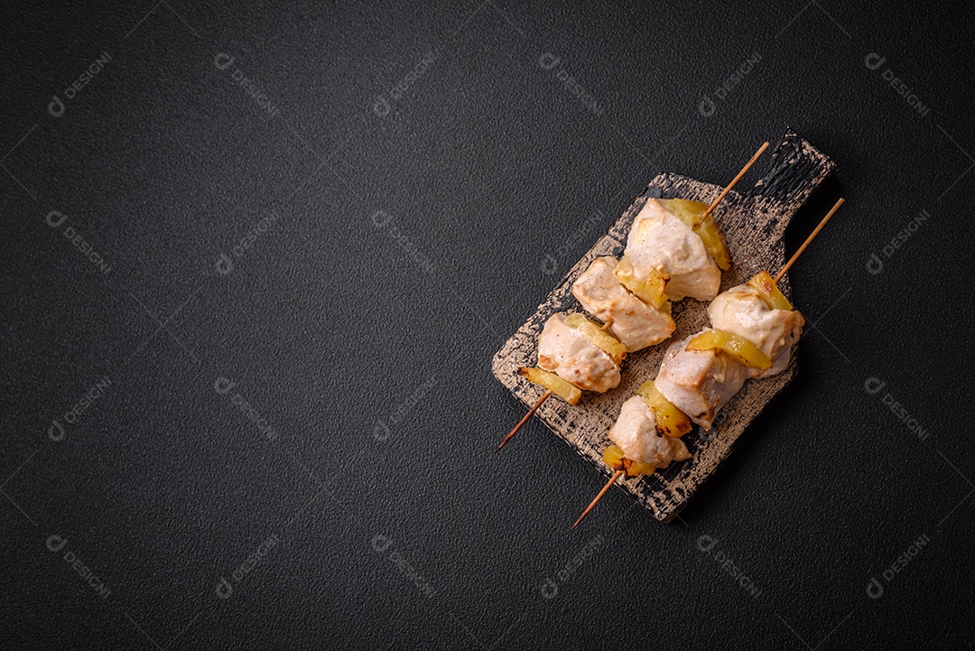 Delicioso kebab de frango ou peru com pedaços de abacaxi em espetos com sal, especiarias e ervas em um fundo escuro de concreto