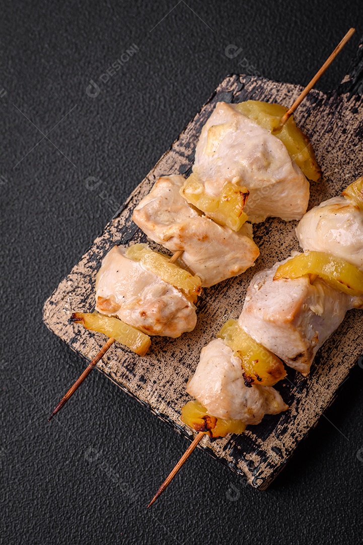 Delicioso kebab de frango ou peru com pedaços de abacaxi em espetos com sal, especiarias e ervas em um fundo escuro de concreto