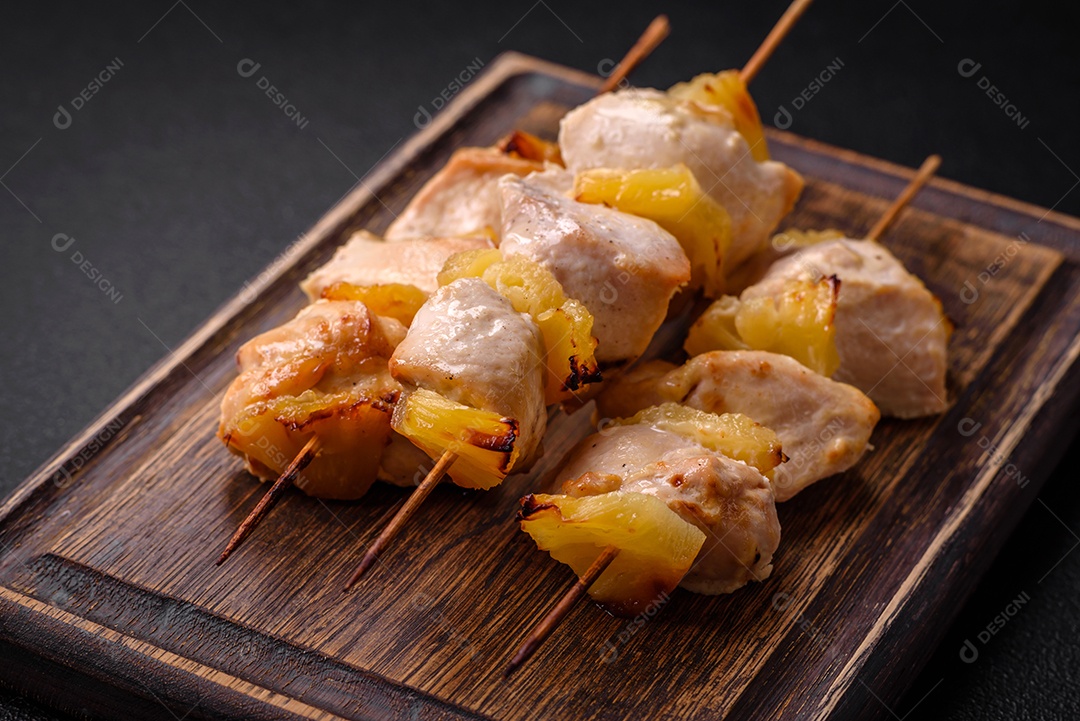 Delicioso kebab de frango ou peru com pedaços de abacaxi em espetos com sal, especiarias e ervas em um fundo escuro de concreto