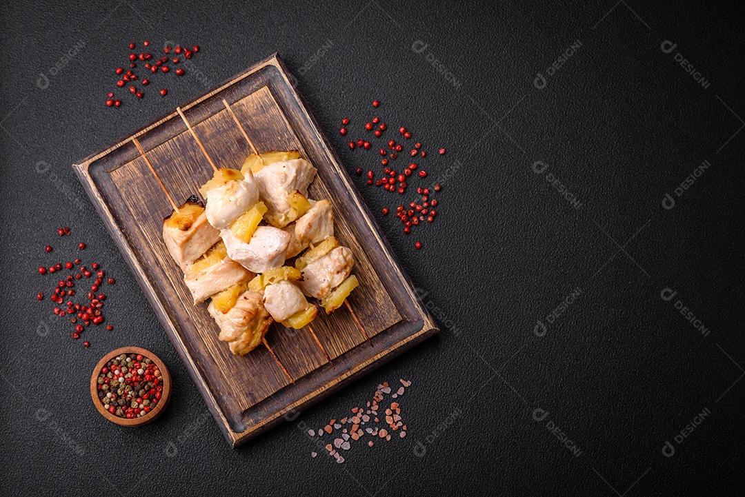 Delicioso kebab de frango ou peru com pedaços de abacaxi em espetos com sal, especiarias e ervas em um fundo escuro de concreto
